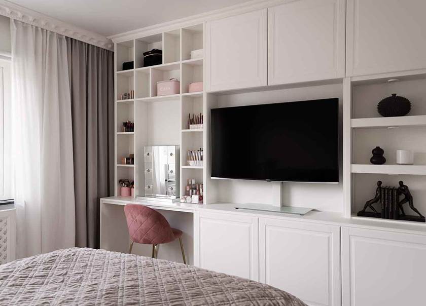 Inbyggd bokhylla i sovrum, med plats för sminkbord med rosa stol framför.