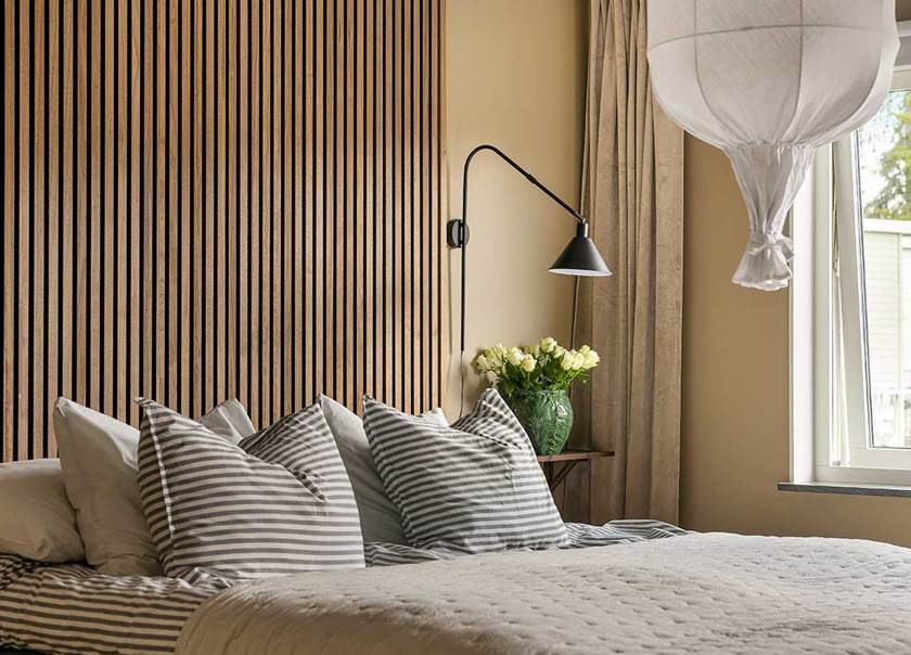 Dubbelsäng med grå sängkläder framför en sänggavel av akustikpanel.