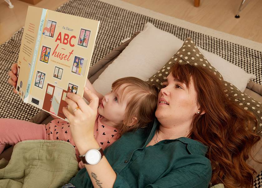Kvinna läser bok för barn liggande på golvet.