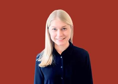 porträtt av Anna Berggren BoKlok, blond kvinna i mörkblå skjorta mot röd bakgrund porträtt av Anna Berggren BoKlok, blond kvinna i mörkblå skjorta mot röd bakgrund