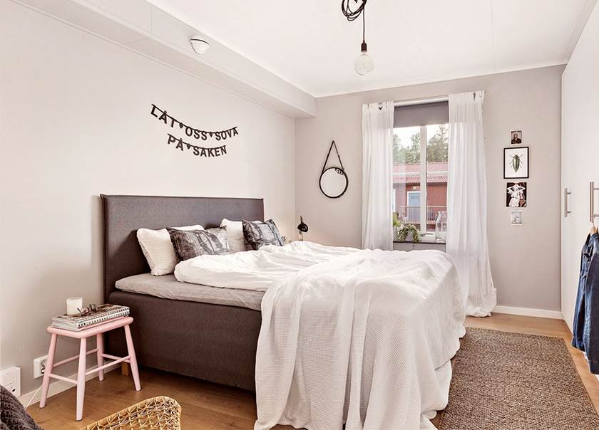 Säng med grå sänggavel i vitt sovrum med ordspråk hängande över sängen