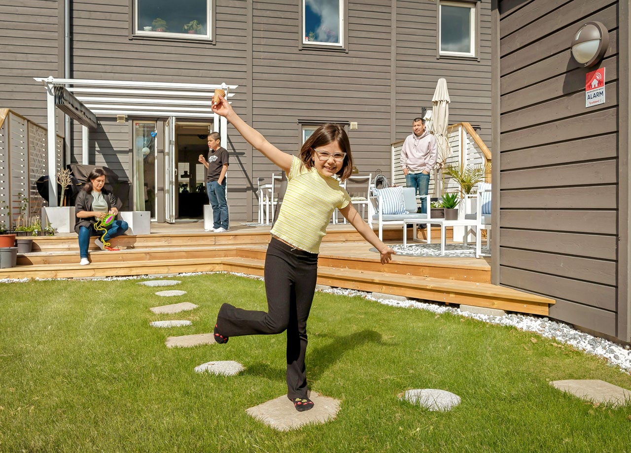 Flicka leker i trädgården utanför sitt grå radhus.