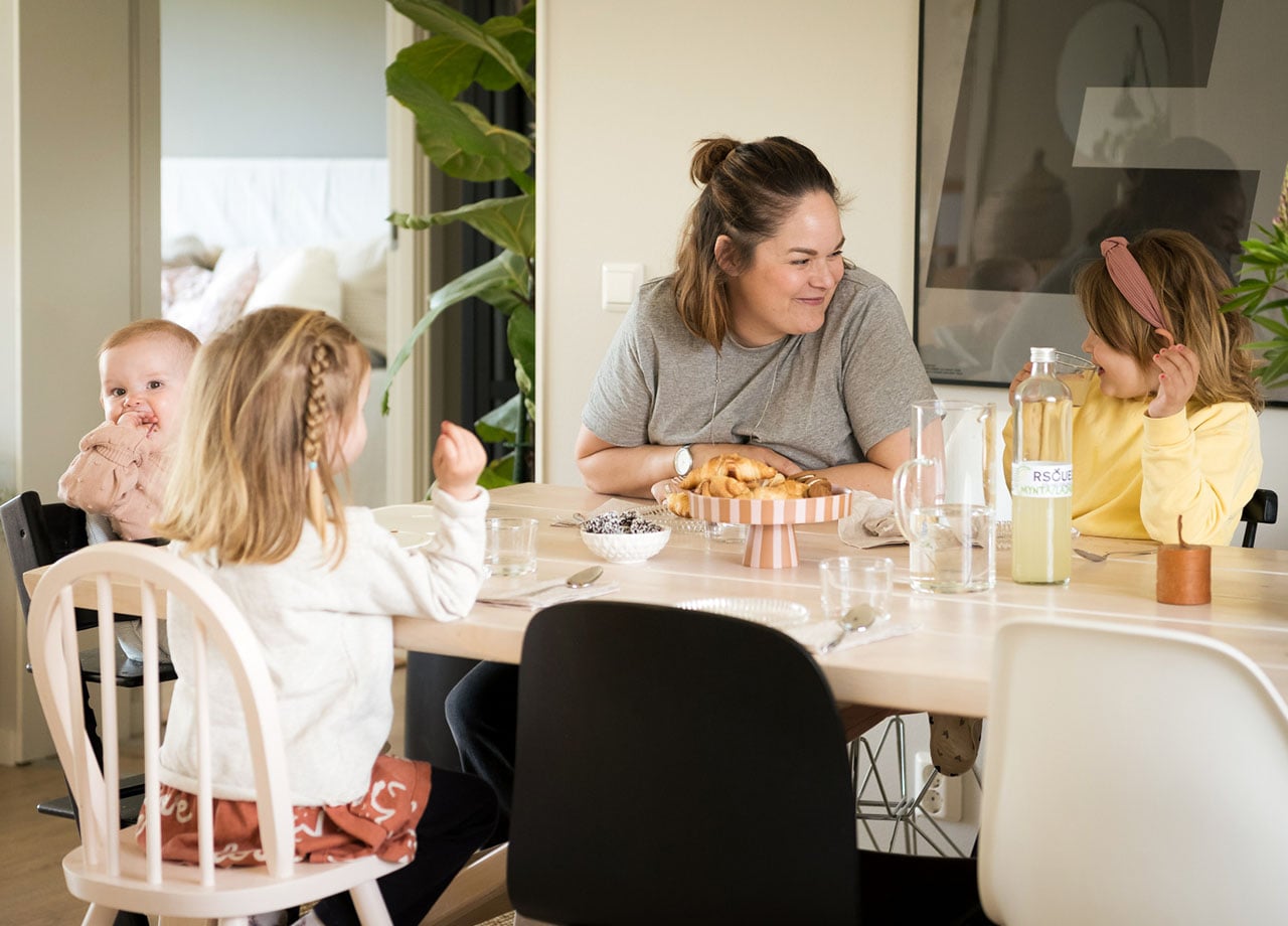 Familj med mamma och tre barn fikar vid matbord.