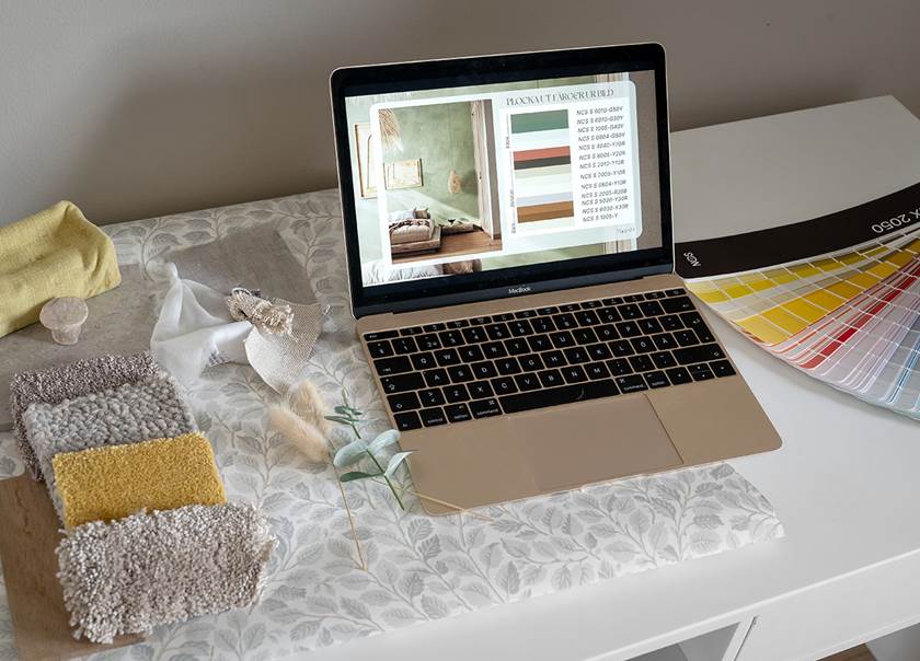 Laptop på skrivbord med färgprover och tygprover.