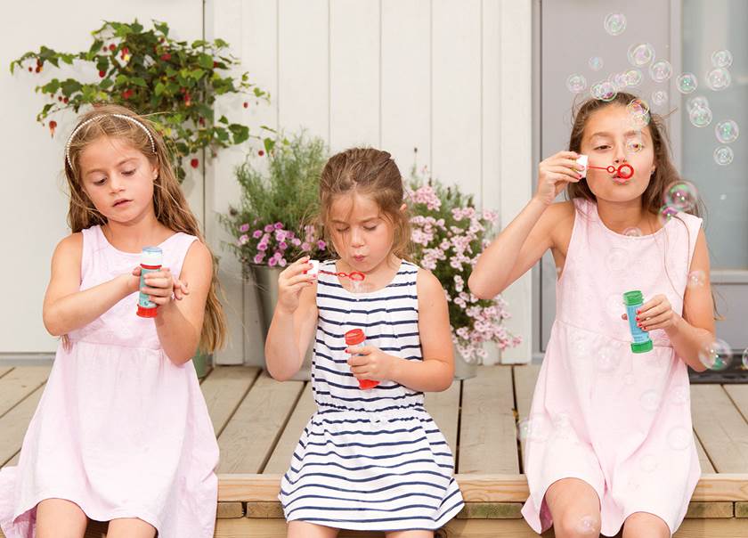 tre flickor i sommarklänningar sitter på kanten till en loftgång och blåser såpbubblor