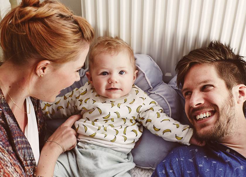 en mamma och pappa leker med sin bebis i sängen