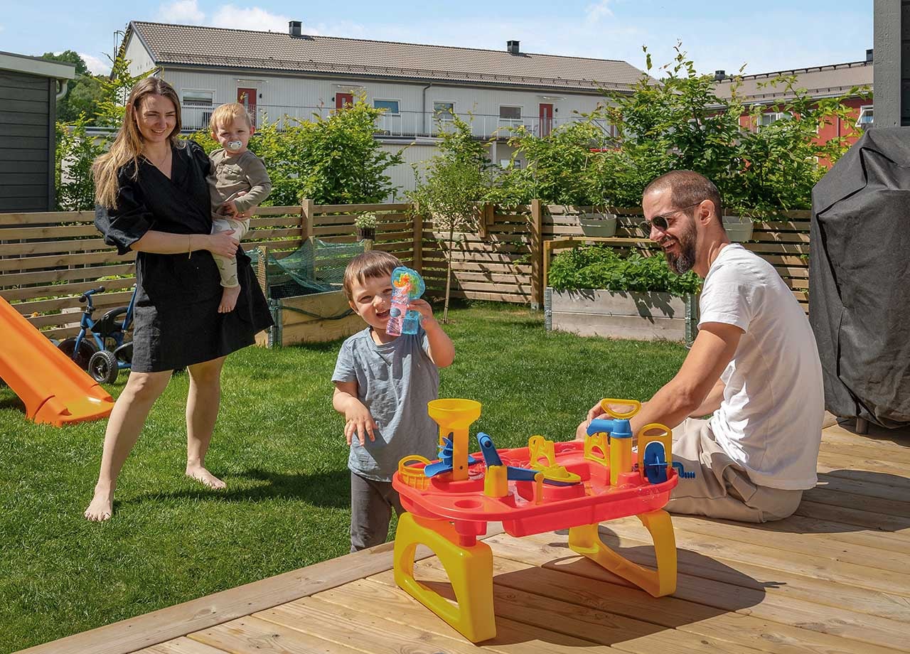 Familj med två vuxna och två barn på altan med trädgård.