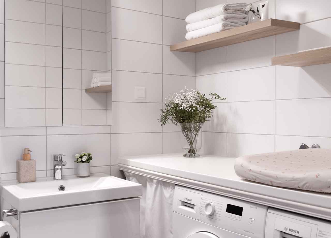 Handfat och tvättmaskin i badrum med vas med blommor i