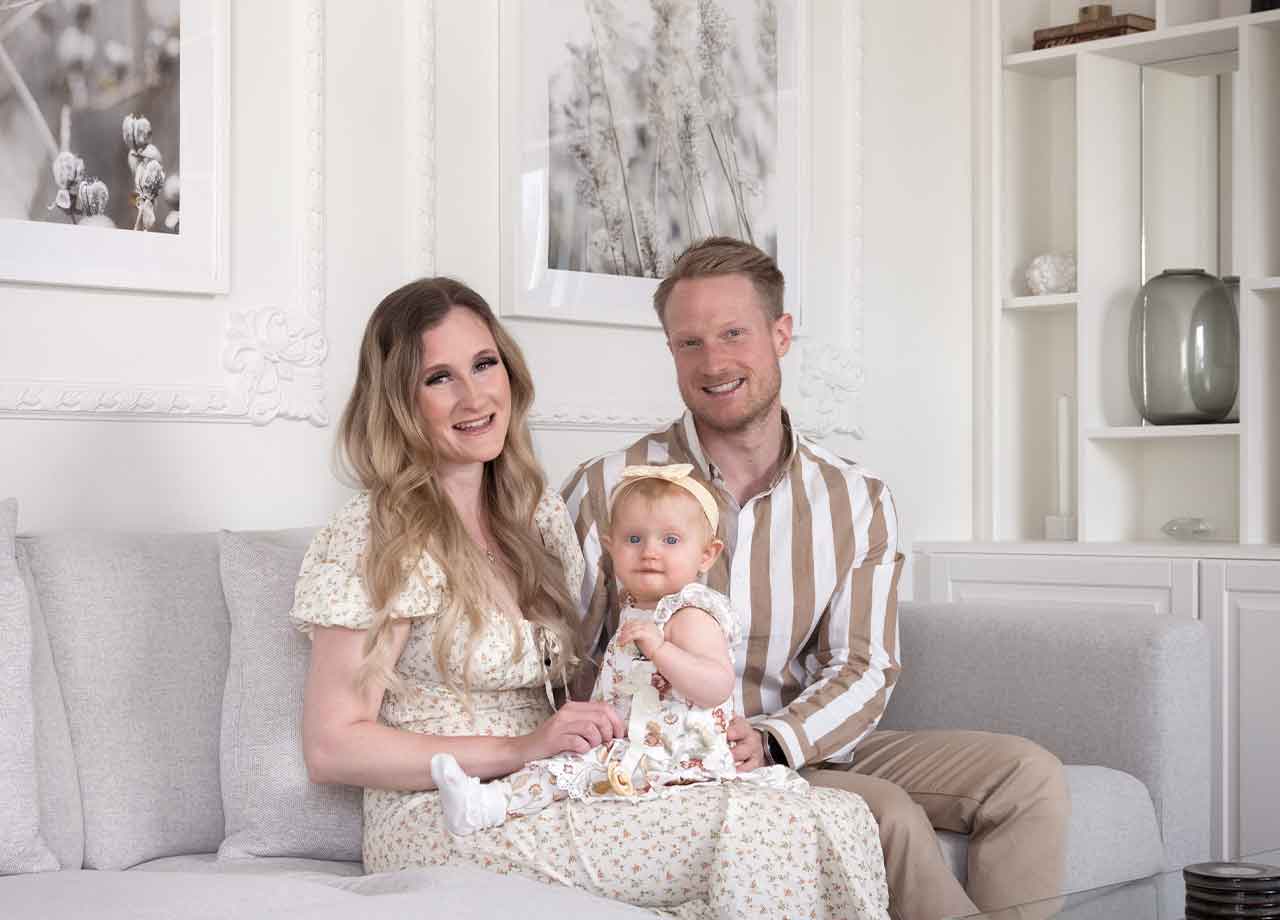 Familj med mamma, pappa och liten dotter som sitter i grå soffa