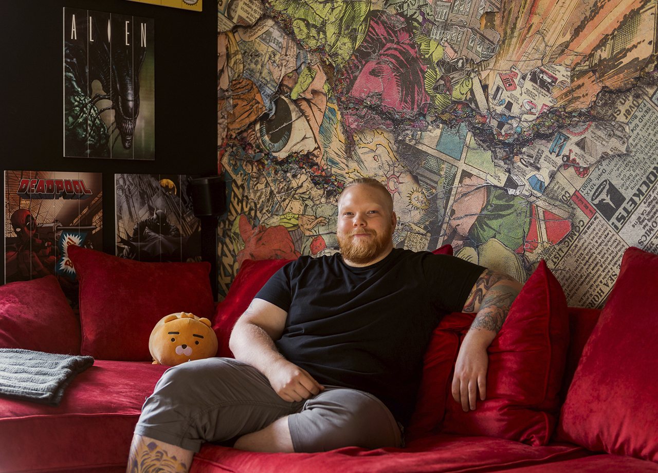 Man i röd soffa framför vägg med seriefigurer