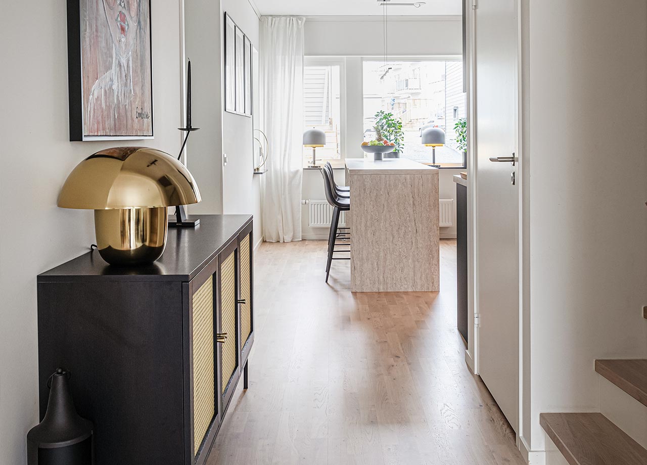 Svart skåp med lampa i guld i gång mellan kök och vardagsrum