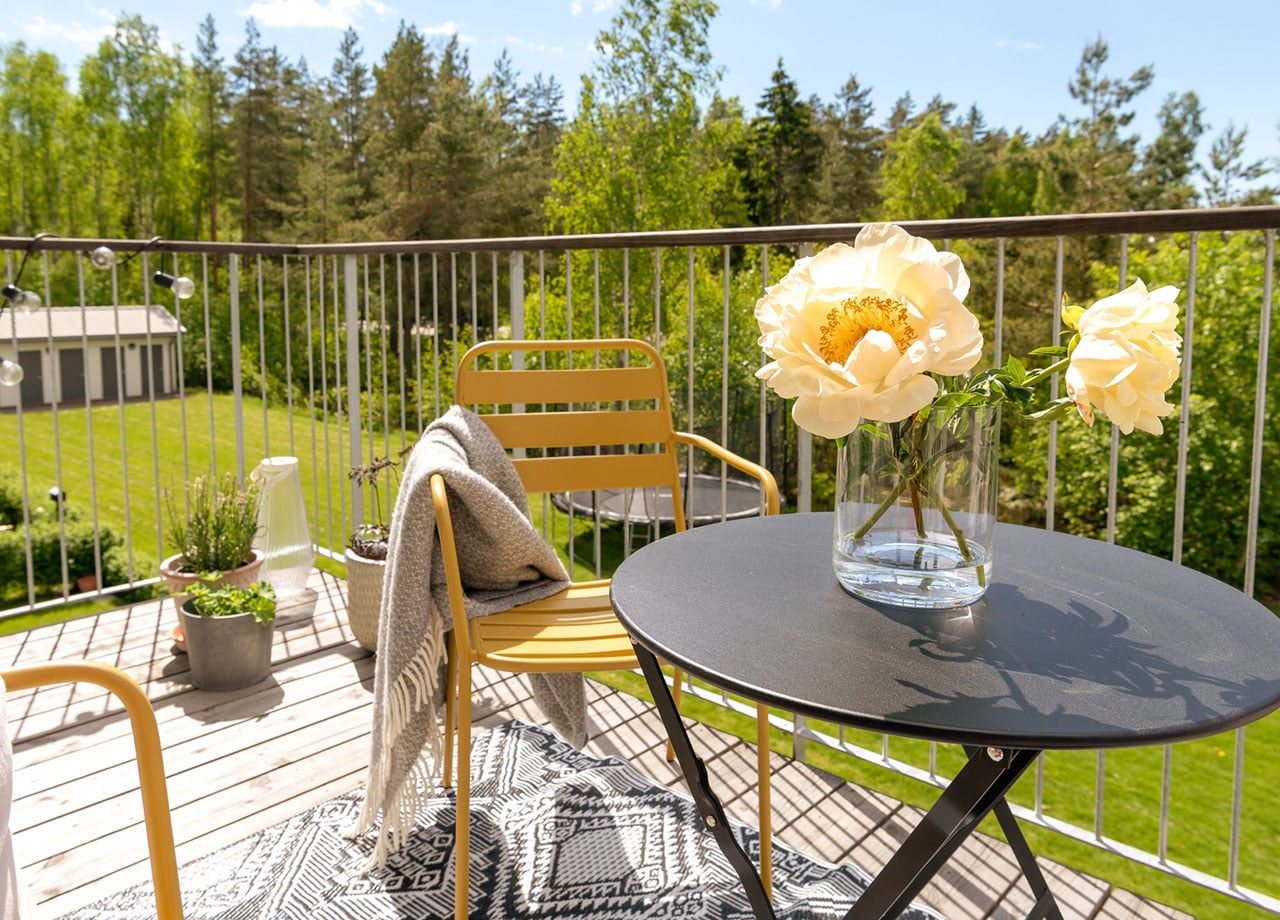 Balkong med svart bord och gul stol med gul blomma i vas på bordet