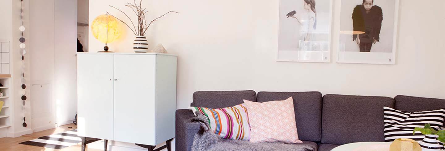 Vardagsrummet med svart soffa tavlor på väggen och skåp intill soffan Vardagsrummet med svart soffa tavlor på väggen och skåp intill soffan