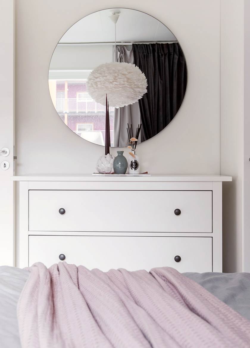 Vit byrå med spegel ovanför där taklampa i vita fjädrar reflekteras. Vit byrå med spegel ovanför där taklampa i vita fjädrar reflekteras.