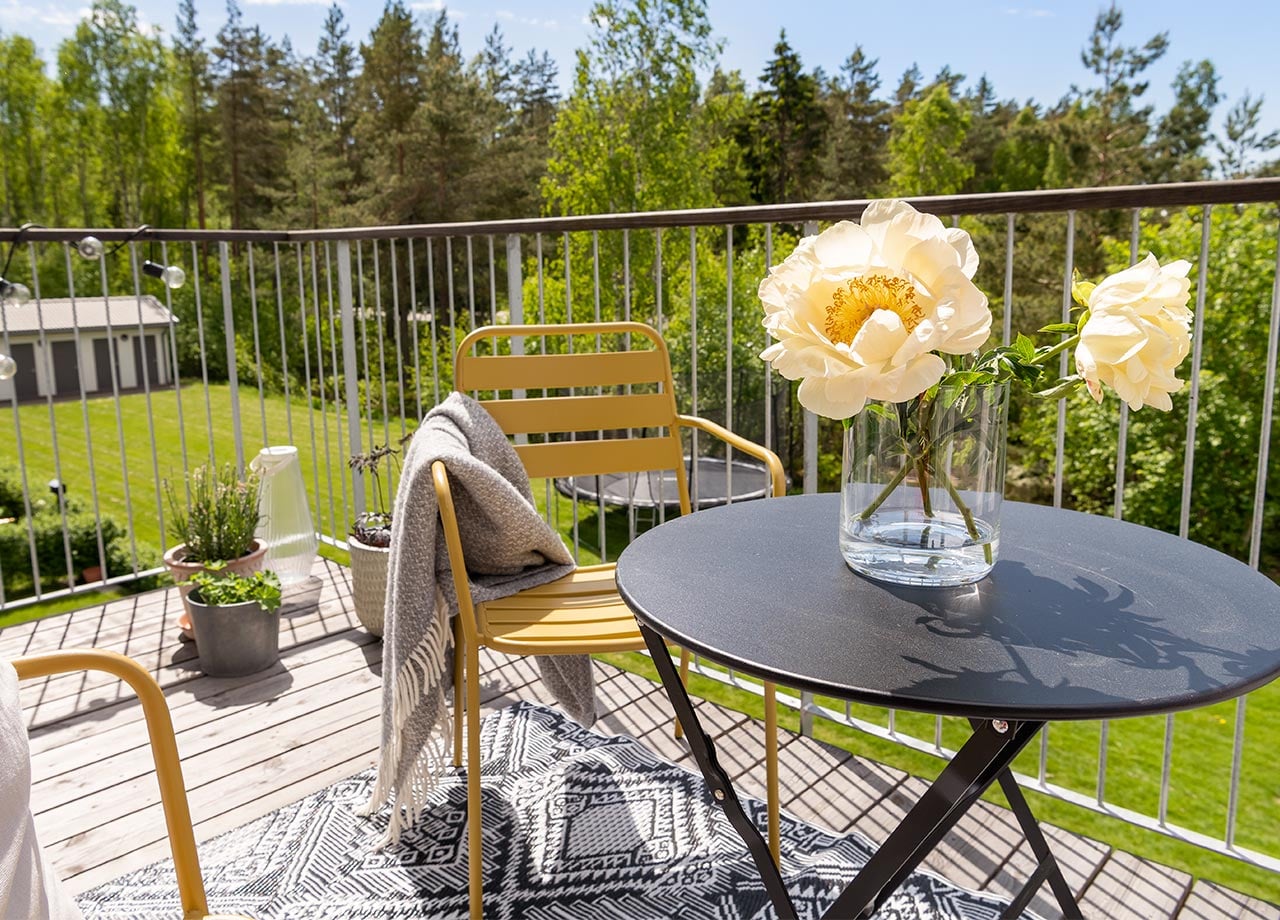Solgul balkongstol och svart runt bord med stora gula blommor i vas.