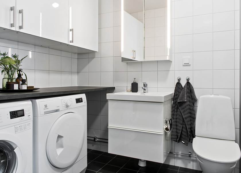Badrum med tvättmaskin och torktumlare med vitt kakel och mörkgrått klinker