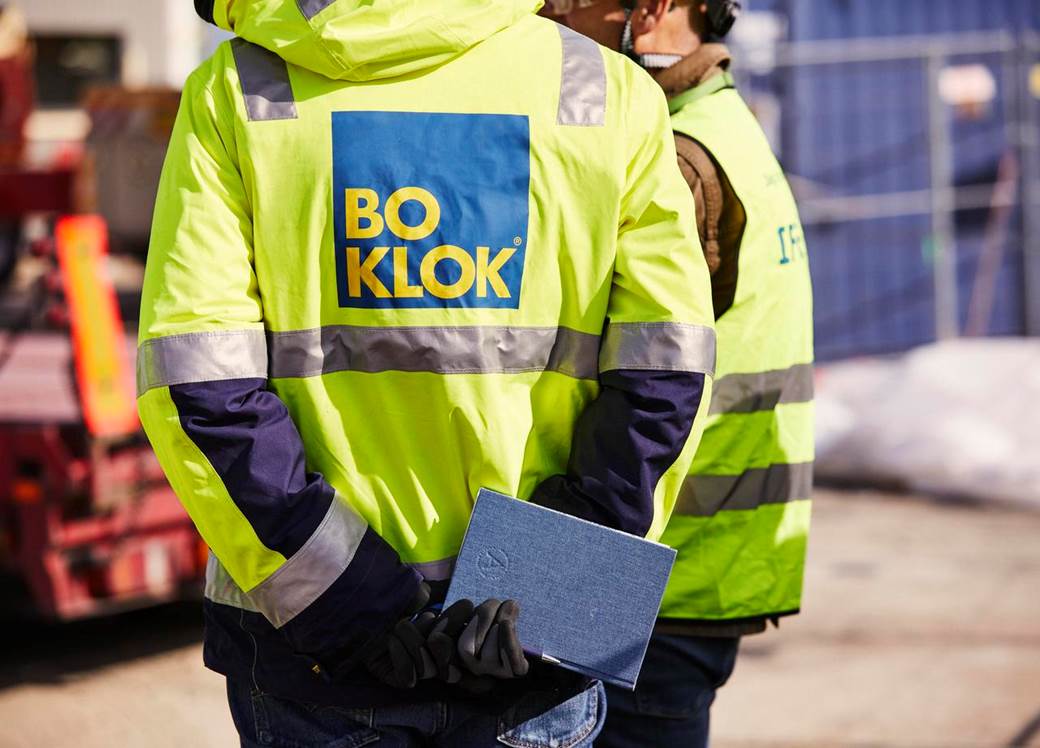 BoKlok personal på byggarbetsplats med skyddskläder håller anteckningsbok och penna bakom ryggen