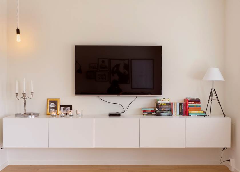 TV som hänger över TV bänk med lampa och böcker på