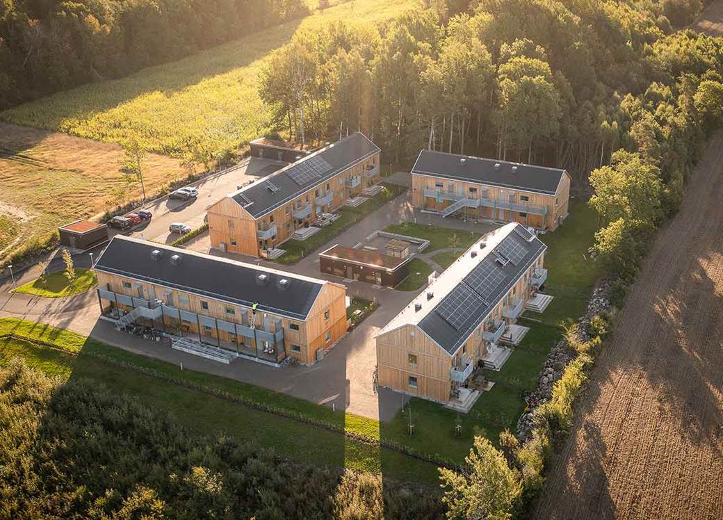 Fyra flerfamiljshus i trä runt en innergård med gröna ytor.
