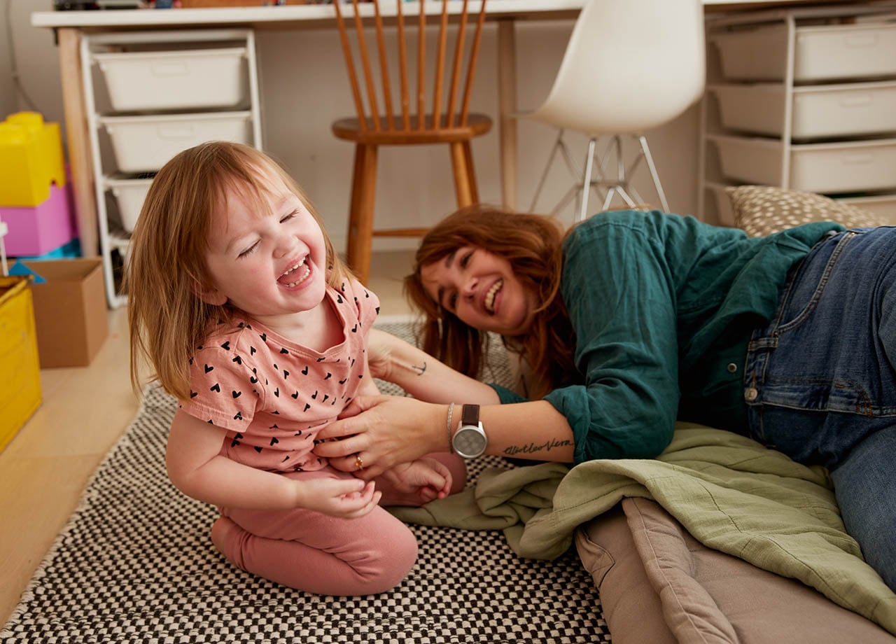 Mamma och dotter leker på golvet och skrattar.