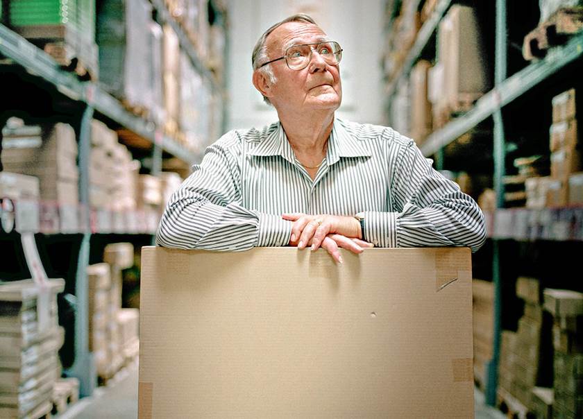 Bild på Ingvar Kamprad som står och ser tänkande ut lutandes med armarna på en kartonglåda på ett IKEA ta själv lager