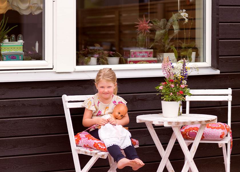 Alma fem år sitter på uteplatsen till sitt BoKlok radhus med bord och stolar med sin docka