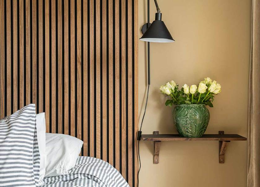 Sovrum med akustikpanel som sänggavel i betsad färg. På hyllan bredvid sängen står en grön vas med gula rosor i.
