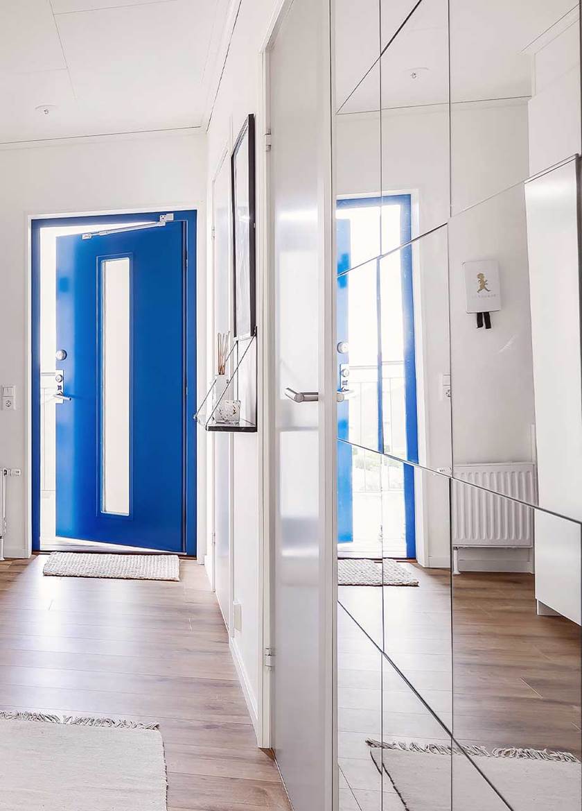 En spegelvägg till höger reflekterar den blå ytterdörren i entrén.