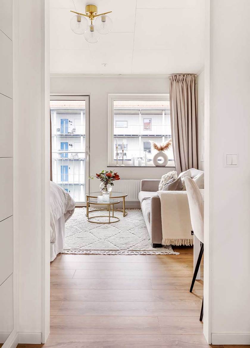 Vy mot ett vardagsrum med beige soffa på vit matta och med fönster och fransk balkongdörr.