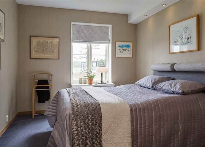 Dubbelsäng med grå sängkläder i sovrum med grå heltäckningsmatta.