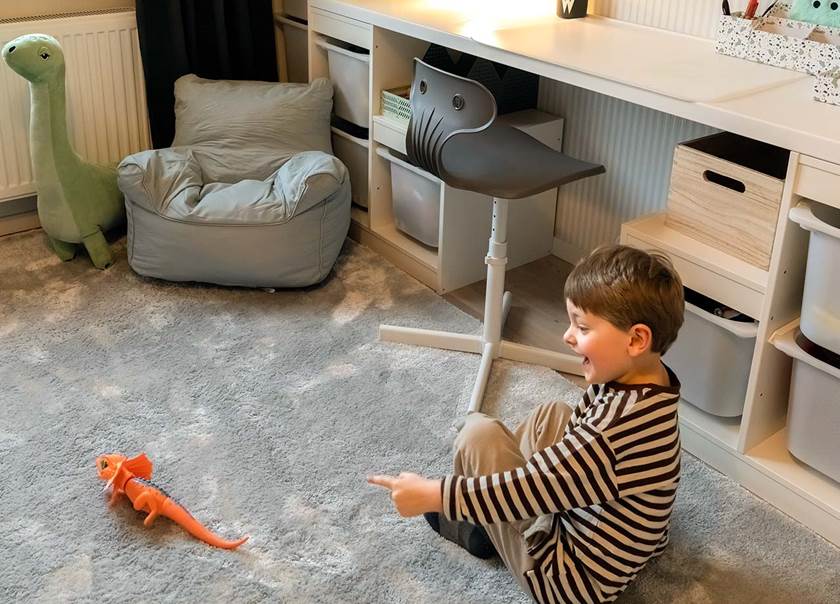 Brunhårig pojke pekar på orange dinosauriedrake på grå matta