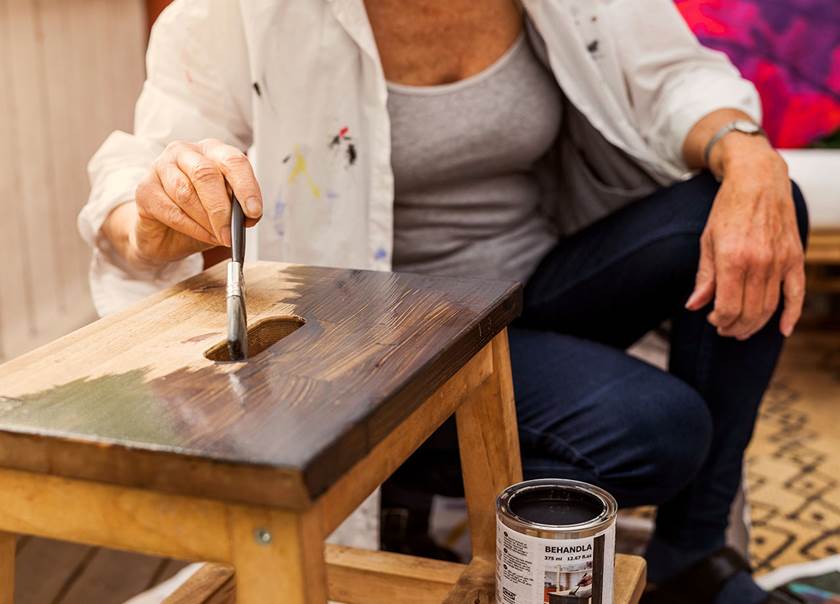 Kvinna sitter på huk och målar en IKEA-pall