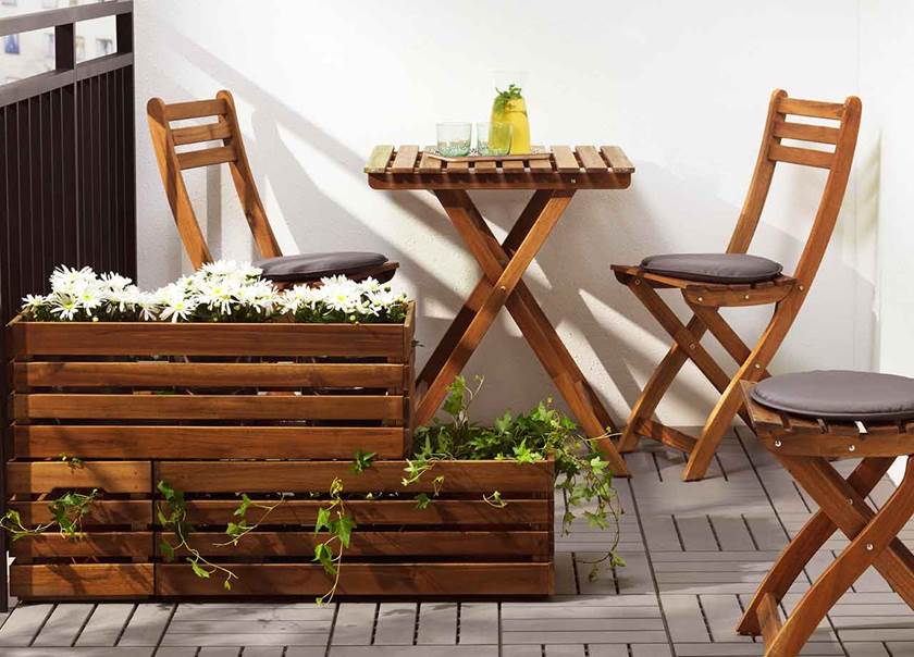 Bruna blomlådor placerade ovanpå varandra med växter i etapper. Bakom står ett brunt bord och bruna stolar på balkongen.