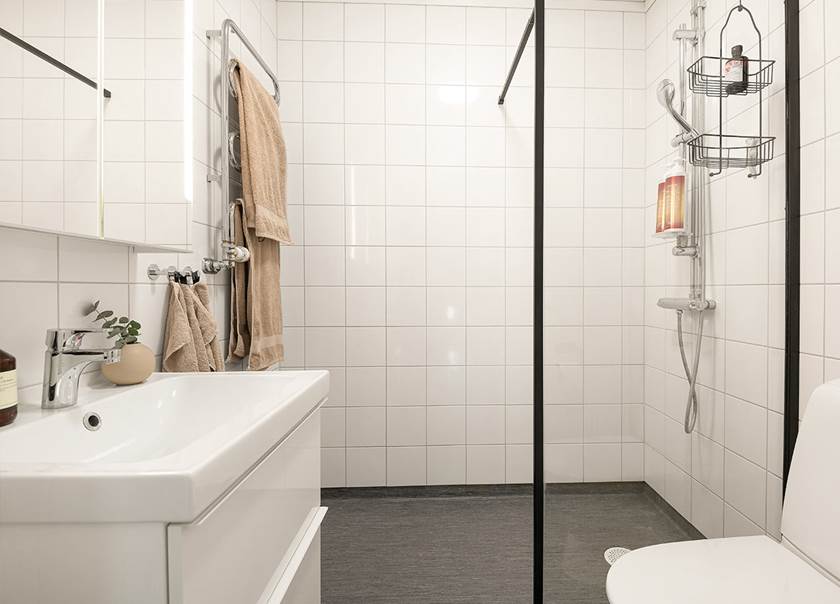 Badrum med duschvägg av klarglas och svart metallram.