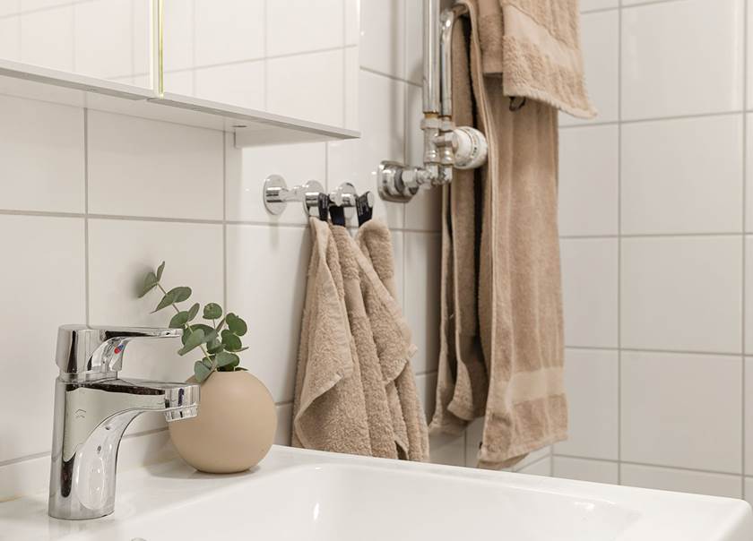 Beige klotvas med eukalyptuskvist på vitt tvättfat bredvid beige handdukar.