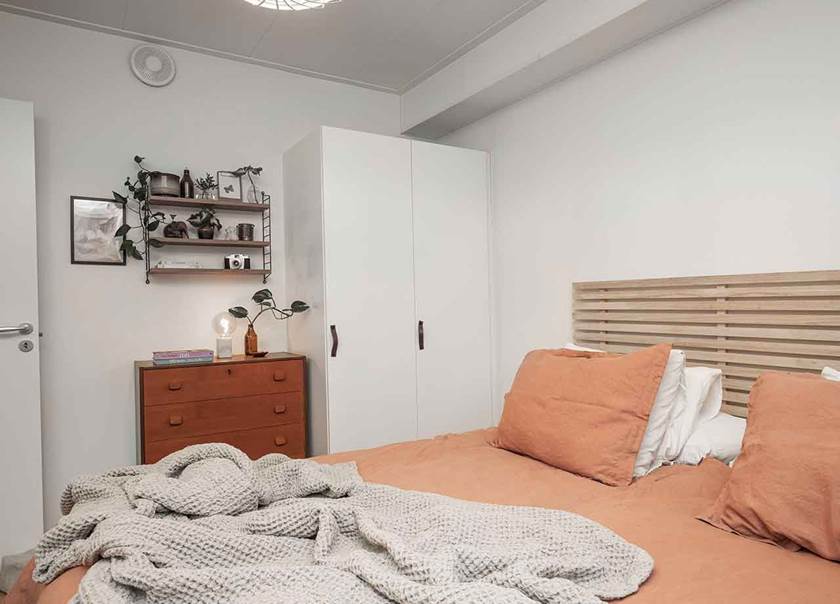 Teakbyrå och vägghylla med klätterväxt i sovrum med dubbelsäng med aprikosfärgade sängkläder