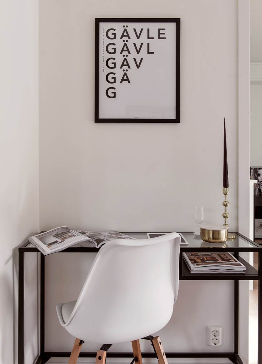 Vit stol vid skrivbord Vittsjö från IKEA, med svart ram och bordsskiva i klarglas. Tavla med bokstäverna Gävle.