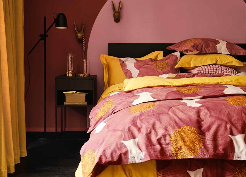 Rum med rosa väggar, gula långa gardiner och säng bäddad med blommönstrat påslakan i rosa, orange och gult
