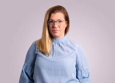 Foto av kvinna i långt blont hår, glasögon och med ljusblå blus.