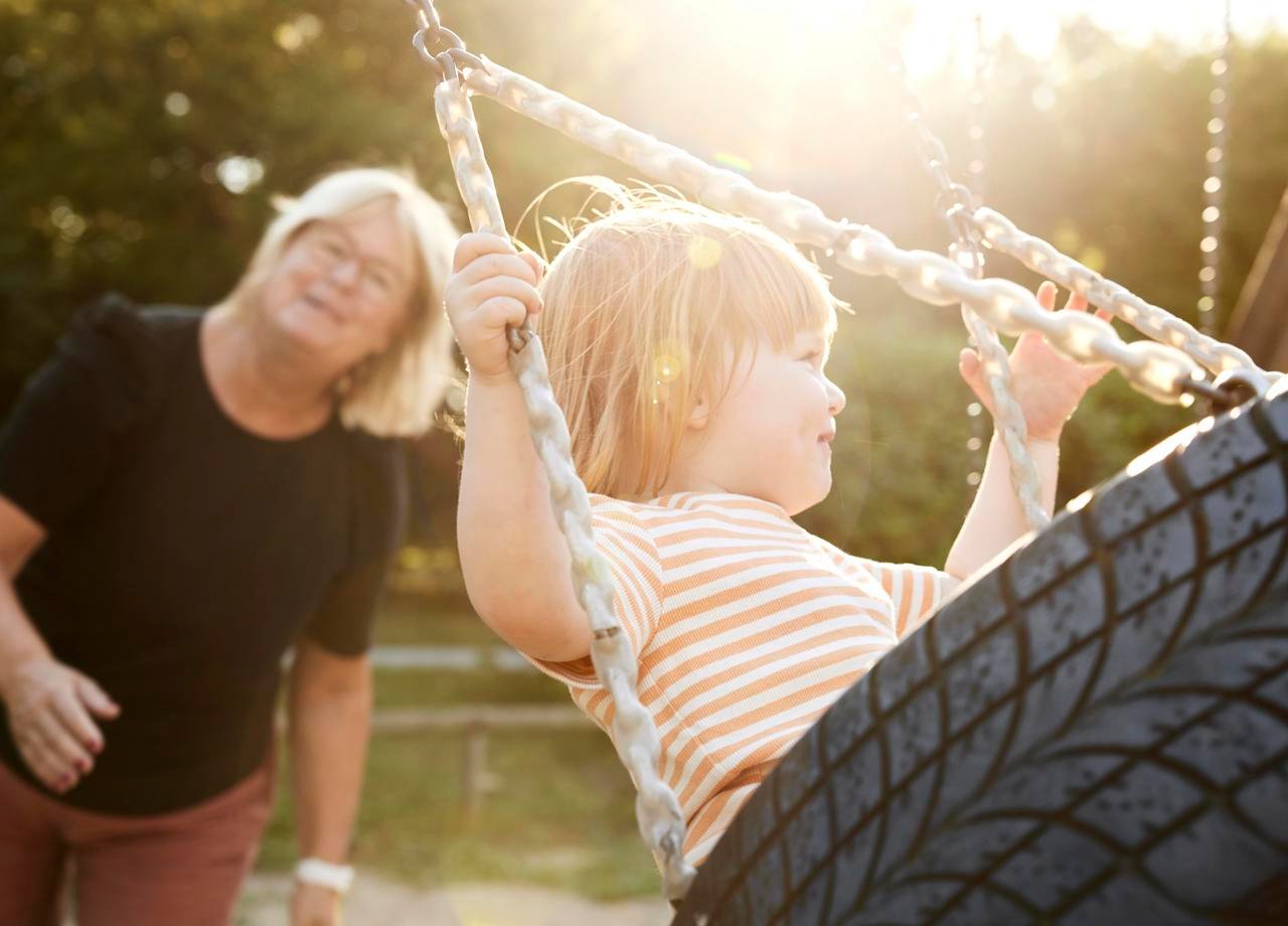 Foto på ett barn som blir gungat av sin mormor eller farmor