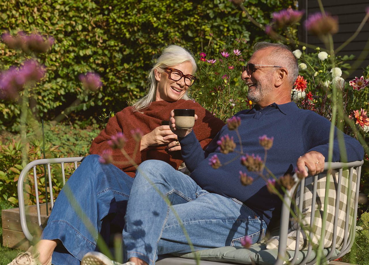 Man och kvinna sitter utomhus och dricker kaffe i soffa.