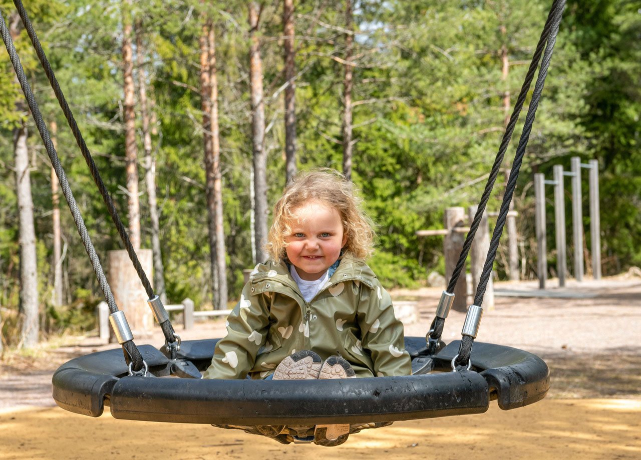 Flicka med lockigt hår som gungar på lekplats