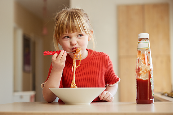 Flicka sitter vid matbord och äter spaghetti  med ketchup