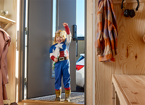 Flicka utklädd till superhjälte står i dörröppning