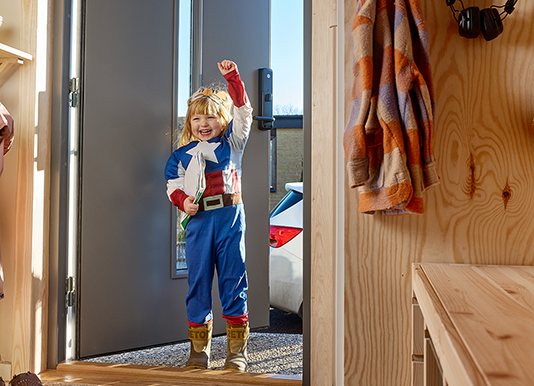 Flicka utklädd till superhjälte står i dörröppning