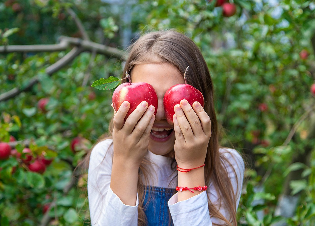 Flicka håller röda äpplen framför ögonen.