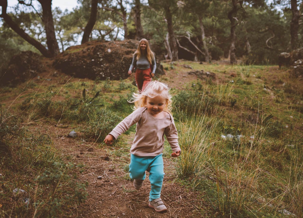 Flicka springer på skogsstig med sin mamma bakom sig.