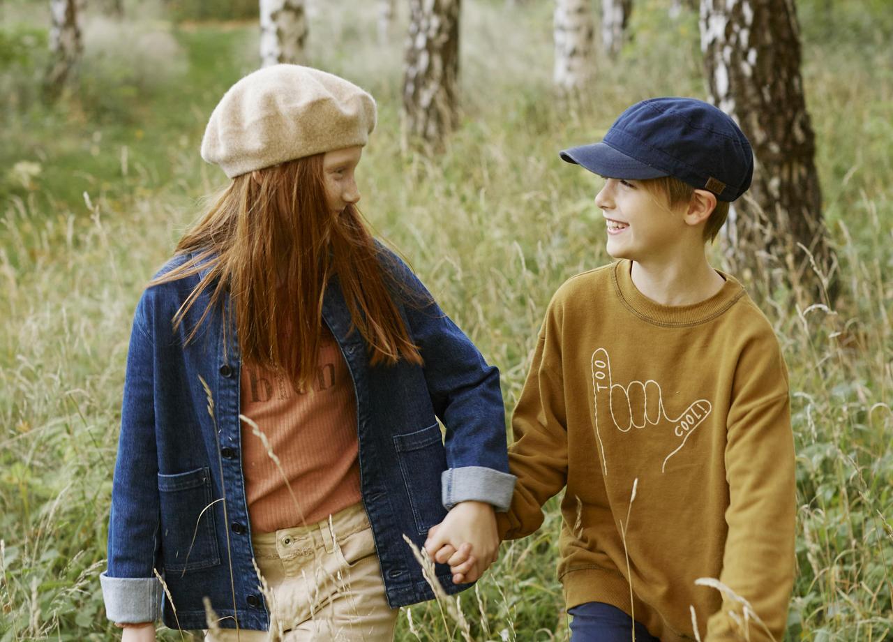 Flicka och pojke håller varandra i handen i högt gräs.