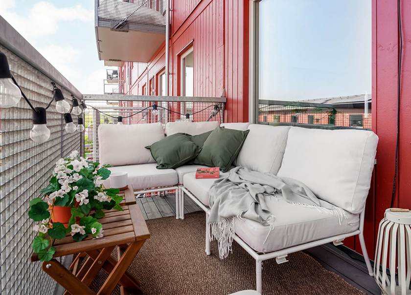 Möblerad balkong till BoKlok lägenhet med röd träfasad.