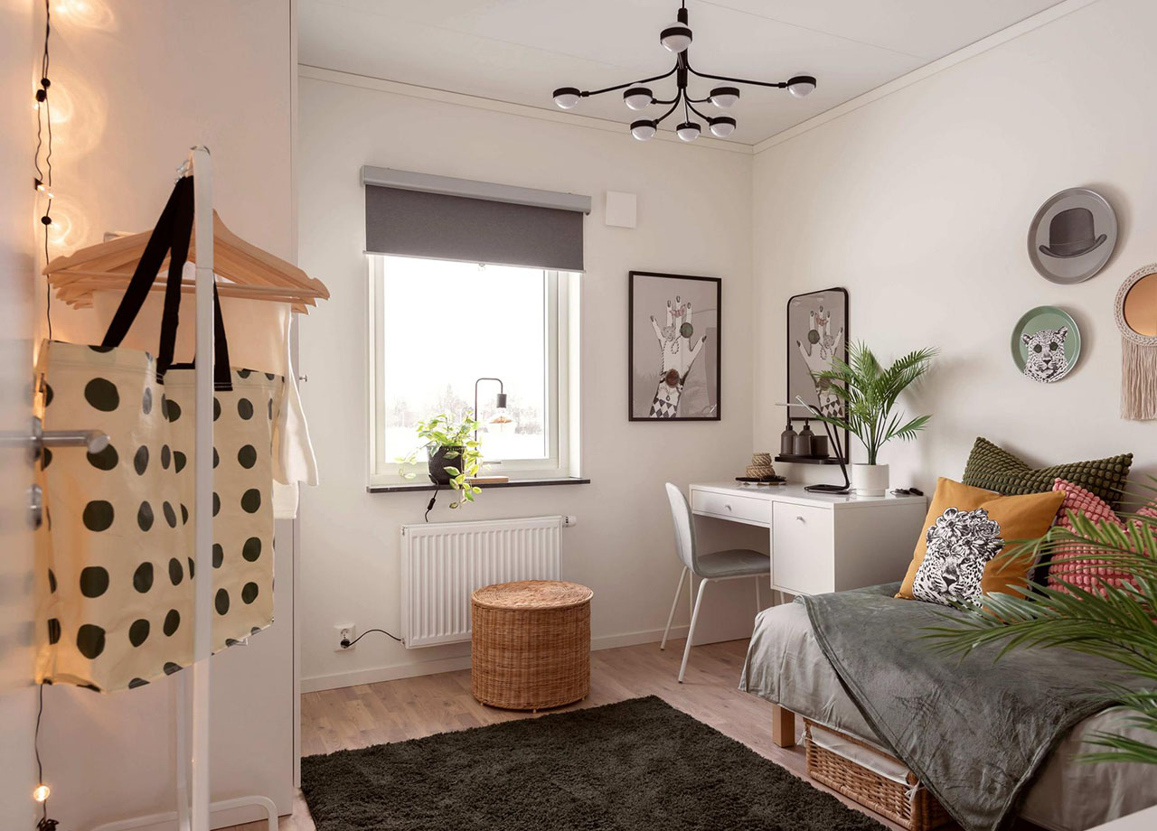 Sovrum med skrivbordshörna kost på väggar och färgglada kuddar i sängen i BoKlok radhus 117 kvm